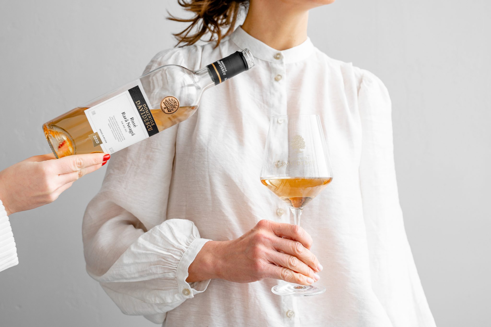 Sticla de vin rose turnata in pahar tinut de o femeie