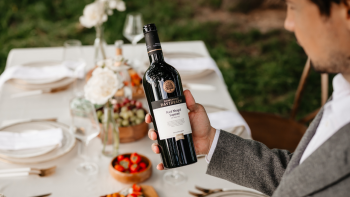 Invitat cu o sticla de Rara Neagra in mana, in fata unei mese afara 